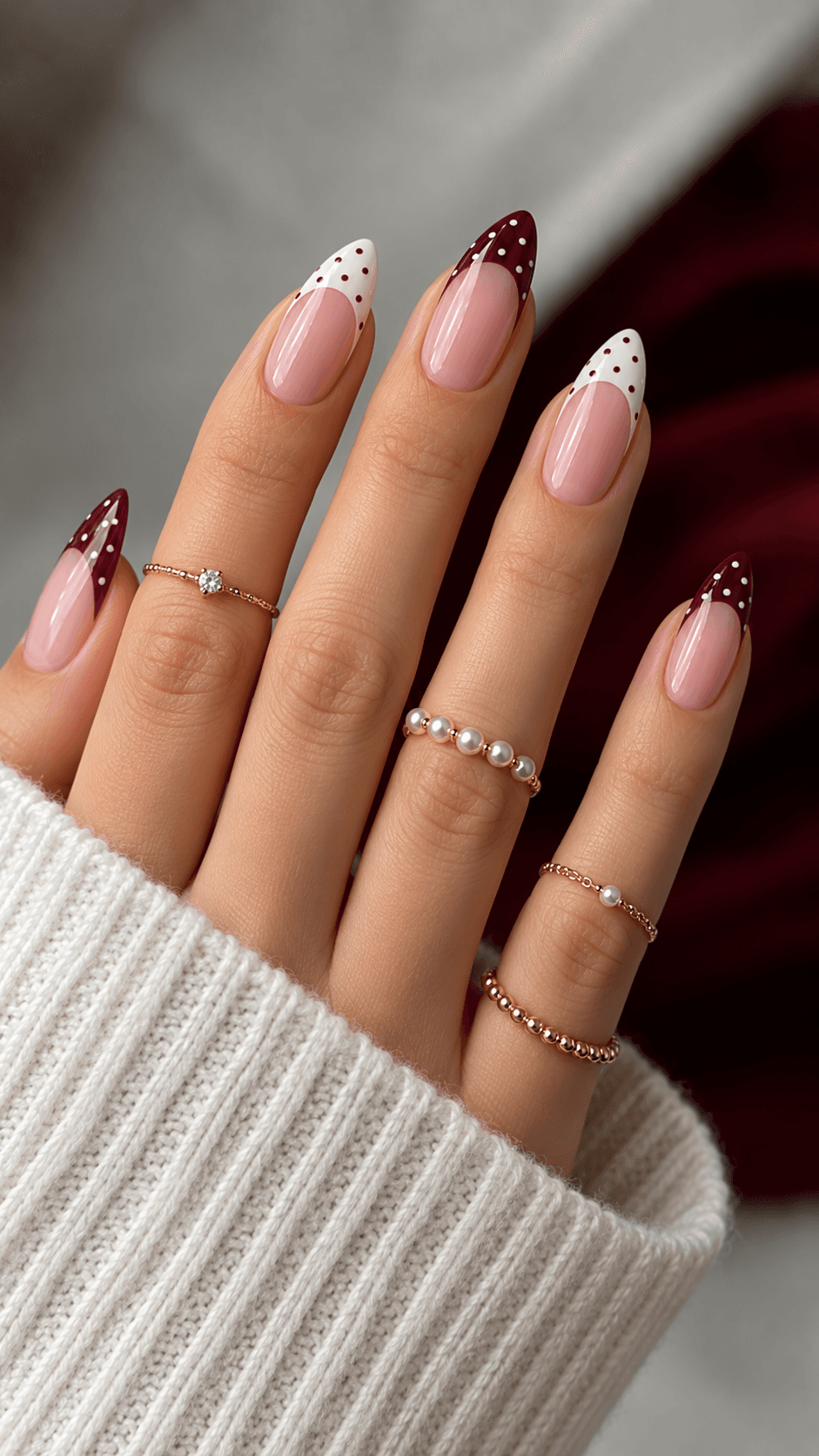 Nude nails with a burgundy and white French manicure and delicate polka-dot detailing, worn with pearl and gemstone rings