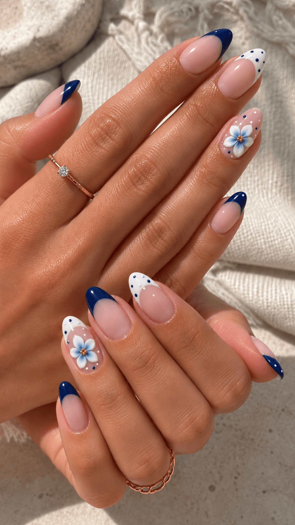 Nude nails with navy French tips and a hand-painted blue and white flower accent, worn in soft natural light