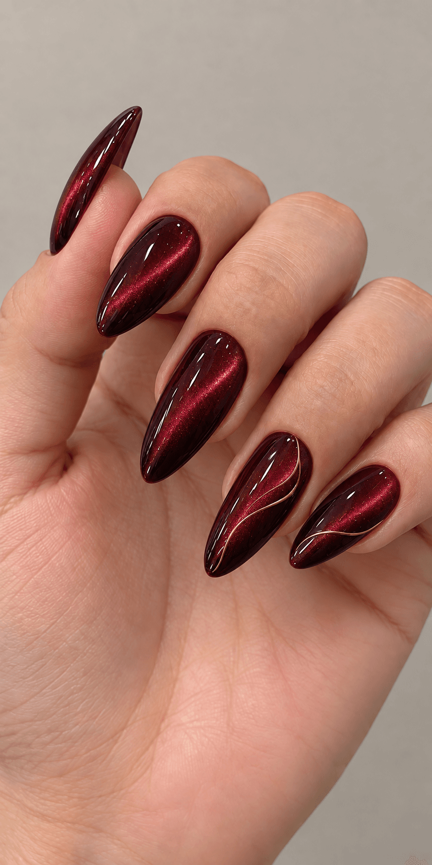 Almond-shaped nails in a deep wine chrome finish with a fine gold swirl accent on two fingers